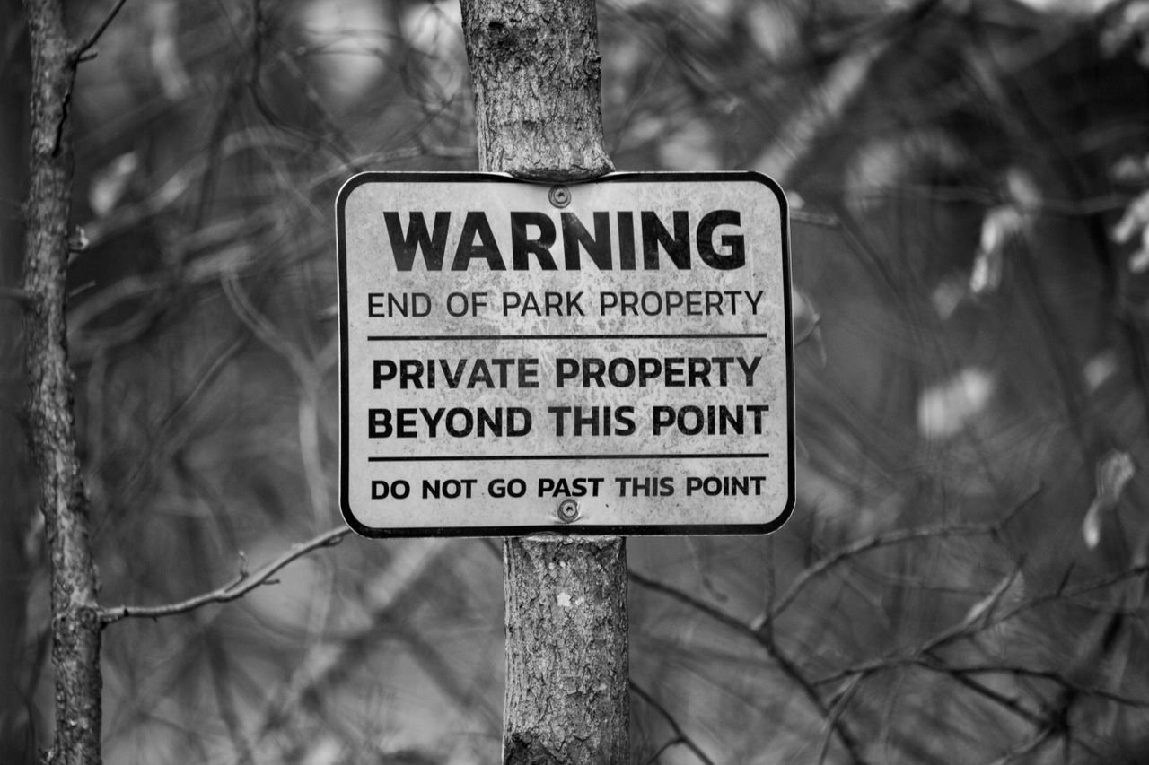 Black and white photo of private property warning sign on tree, forest background.